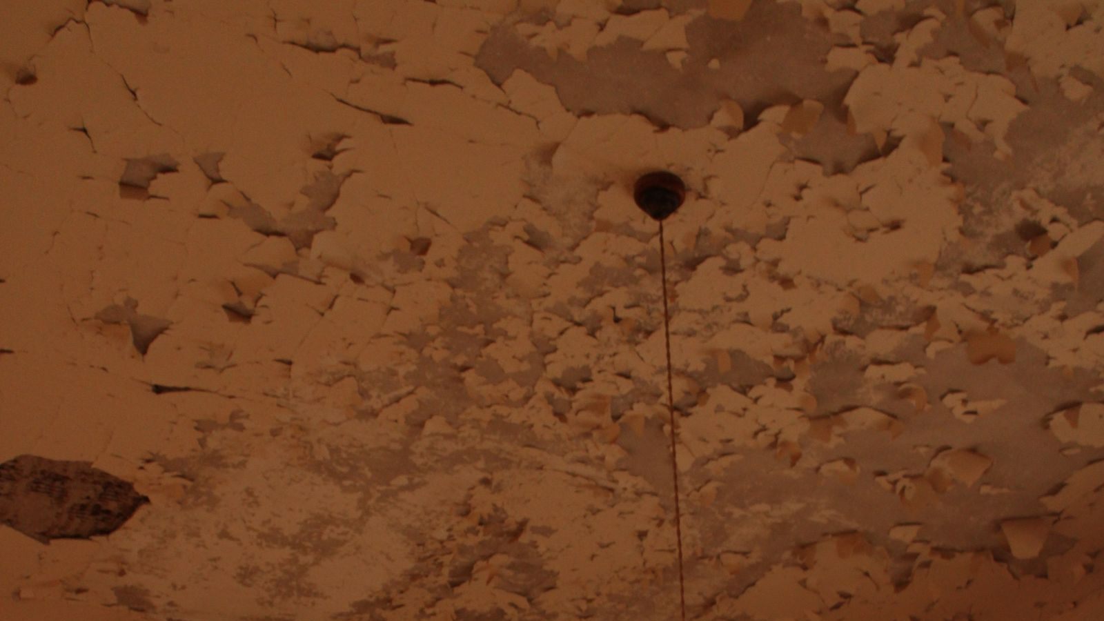 Plafond met vochtschade en bladderende verf rond een lamp